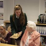 student offering sausage rolls to a woman